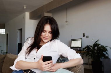 Mutlu Genç esmer kadın oturma odasında kanepede rahatlatıcı akıllı telefon kullanarak