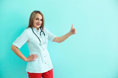 Kendine güvenen kadın doktor stetoskop ve sırt çantası ile başparmak üzerinde mavi arka plan ortaya.