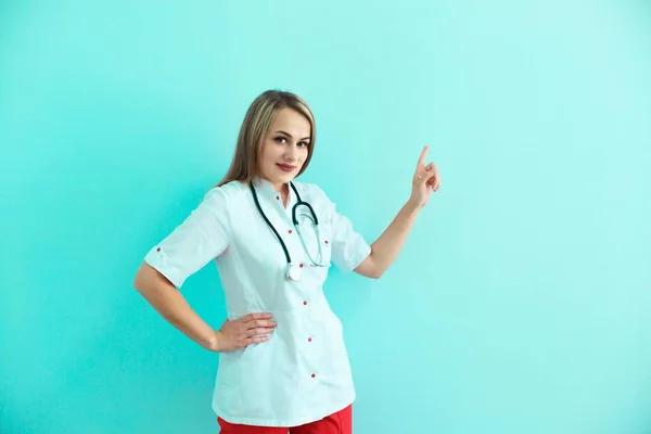 Уверенная женщина-врач со стетоскопом и рюкзаком показывает большой палец на синем фоне . — стоковое фото