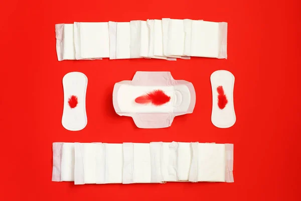 Bulu merah dan pembalut sanitasi dan lembar penyerap pada latar belakang merah — Stok Foto