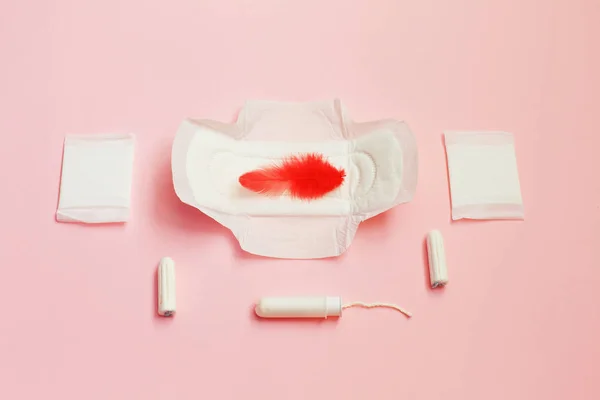 Bulu merah dan pembalut sanitasi dan lembar penyerap pada latar belakang merah muda — Stok Foto