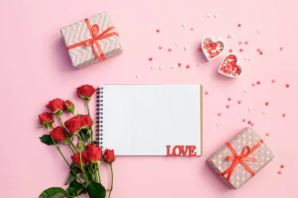 Cuaderno abierto en blanco con caja de regalo, flores y corazones sobre un fondo rosa. Fondo día de San Valentín . — Foto de Stock