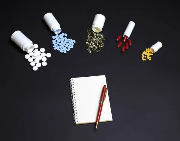 Defter ve kalem siyah arka plan üzerine farklı ilaçlarla — Stok fotoğraf