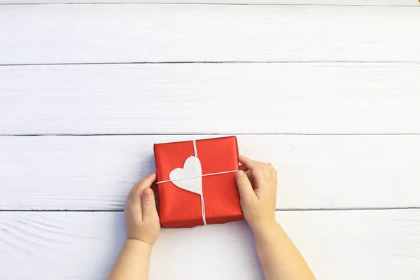 Manos de niño sosteniendo hermosa caja de regalo sobre fondo de madera. Vacaciones, vista luminosa y festiva, puesta plana. Banner de saludo de San Valentín. Día del Padre, Día de la Madre o celebración del Cumpleaños . —  Fotos de Stock