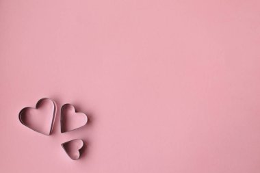 Üç kalp, pembe bir arka plan üzerinde çerez kesici şeklinde. Sevgililer günü.