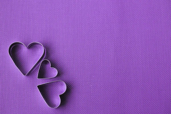 Tres cortadores de galletas en forma de corazón sobre un fondo púrpura . — Foto de Stock