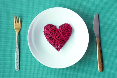Sevgililer günü Festival tablo ayarı. Bir bıçak ve çatal greene arka plan üzerinde beyaz bir plaka üzerinde kırmızı kalp.