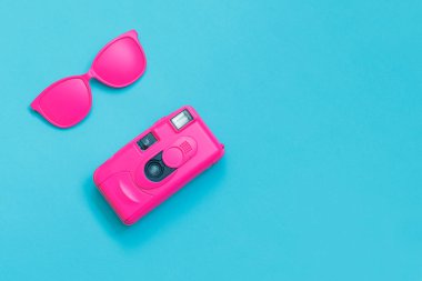 Pembe gözlük ve mavi arka plan üzerinde pembe fotoğraf makinesi. En az kavramı. Yaratıcı kavramı. Sıcak yaz. Pop Art. Parlak tatlı moda stil.