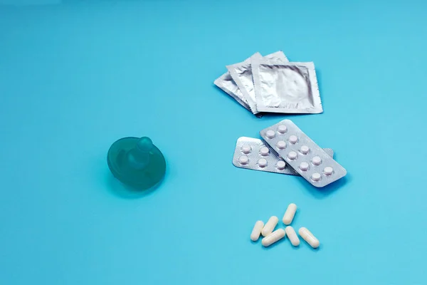 Baby nipple as symbol of pregnancy. Birth control pills and condom on blue background.