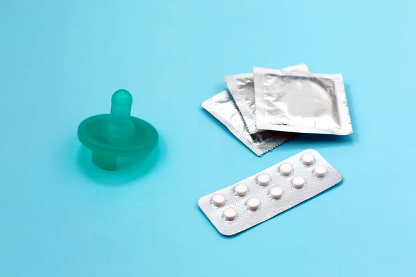 Дитячий сосок як символ вагітності. Таблетки контролю народжуваності та презерватив на синьому фоні . — стокове фото