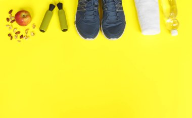 Spor ayakkabı, ip, elma ve su şişe üzerinde sarı arka plan atlama.