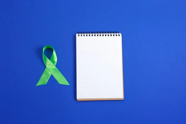 Licht groen lint en notitieblok openen op blauwe achtergrond. Leverkanker lymfoom bewustzijn. Gezondheidszorg en geneeskunde concept. — Stockfoto