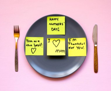 Anneler günü Festival tablo ayarı. Uyarı mektubu sarı etiket üzerinde gri bir tabak bir bıçakla Not ve pembe bir arka plan üzerine çatal