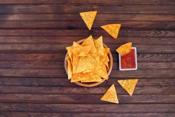 Nachos chips de maíz en un tazón con salsa picante sobre un fondo rústico de madera. Vista horizontal desde arriba — Foto de Stock