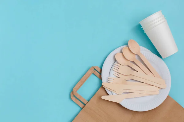 Utensilios desechables ecológicos hechos de madera de bambú sobre una bolsa de papel sobre fondo azul . — Foto de Stock