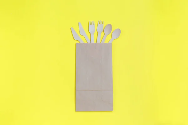 Vajilla desechable de materiales naturales, cucharas de madera, cuchillos y tenedores en una bolsa de papel sobre fondo amarillo. respetuoso del medio ambiente — Foto de Stock