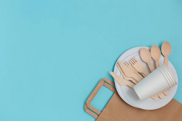 Eco-friendly disposable utensils made of bamboo wood over paper bag on blue background.