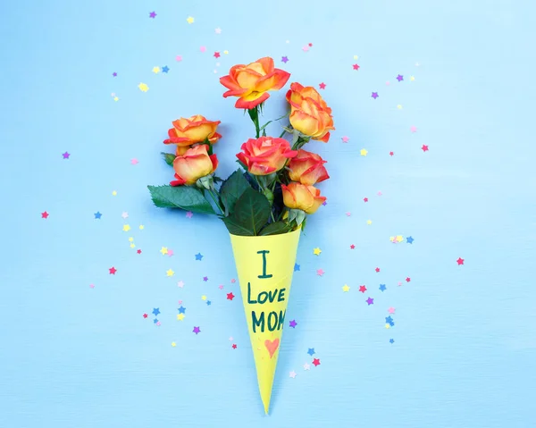 I love mom Mother\'s day. Beautiful fresh vivid orange roses tinged in yellow paper bag on blue background. LOVE MOM message , mother\'s day concept