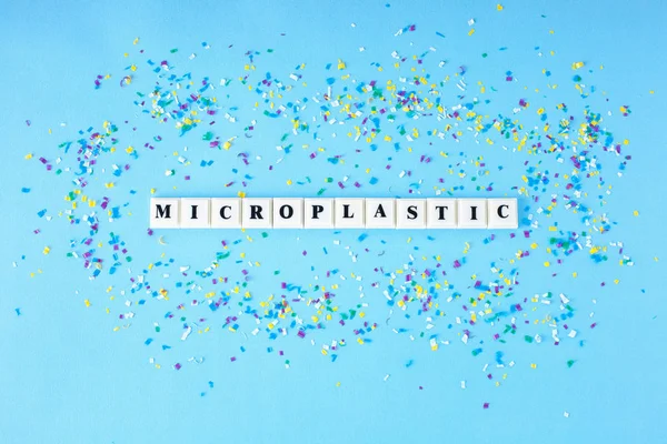 Muovi lohko kuutio sana MICROPLASTIC noin pieniä muovihiukkasia sinisellä pohjalla. Konsepti Mikromuovi vedessä ja elintarvikkeissa . — kuvapankkivalokuva