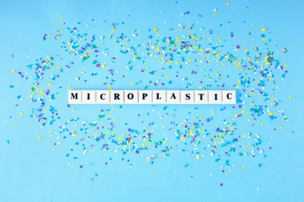 Plastik blok küp mavi bir arka plan üzerinde küçük plastik parçacıklar çevresinde Microplastic kelime ile. Kavram Microplastic su ve gıda.
