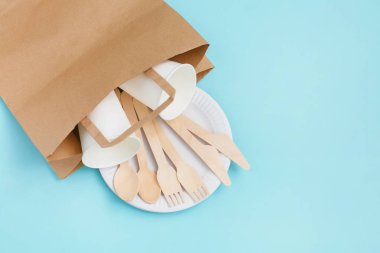 Bambu ahşap kağıt torbaya mavi zemin üzerine yapılan çevre dostu tek kullanımlık mutfak eşyaları.