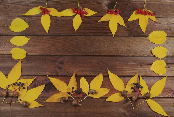 Vintage autumn border from fallen leaves and chestnuts on the old wooden table.