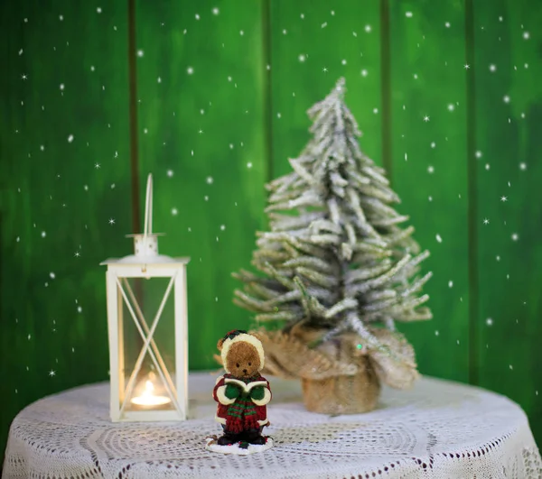 Christmas Decoration with a lighted candle and a Christmas tree and a statue of a bear singing Hymns on a green wooden background. — Stock Photo, Image