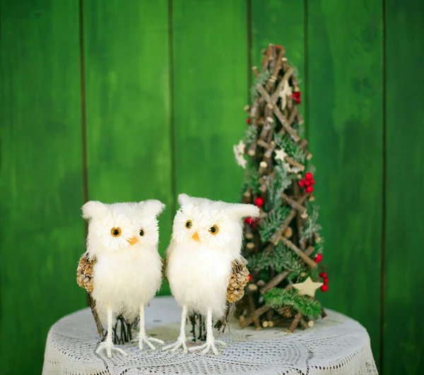 Zwei Weihnachtseulen auf einem Tisch neben einem dekorativen Weihnachtsbaum auf grünem Hintergrund. Vorlage für Neujahrskarten. — Stockfoto