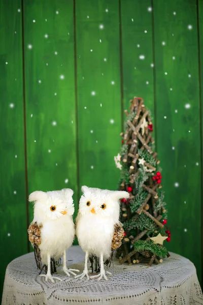 Zwei Weihnachtseulen auf einem Tisch neben einem dekorativen Weihnachtsbaum auf grünem Hintergrund. Vorlage für Neujahrskarten. — Stockfoto