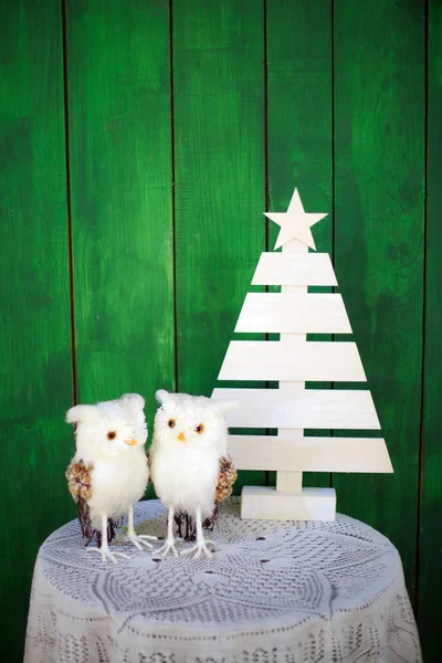 Zwei Weihnachtseulen auf einem Tisch neben einem dekorativen Weihnachtsbaum auf grünem Hintergrund. Vorlage für Neujahrskarten. — Stockfoto