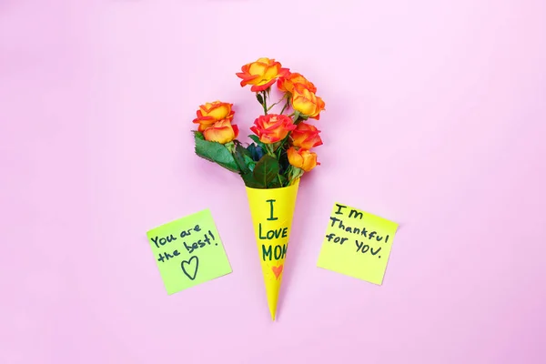 I love mom. Mother\'s day. Note reminder yellow sticker and beautiful fresh vivid orange rose on pink background.