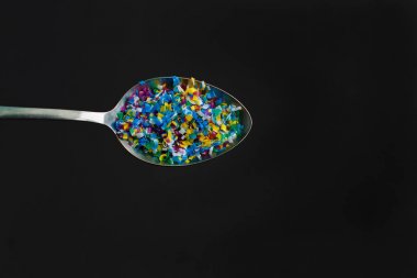 Microplastic in spoon on black background . Threat to human health and environment Dangerous additives Toxic substances.