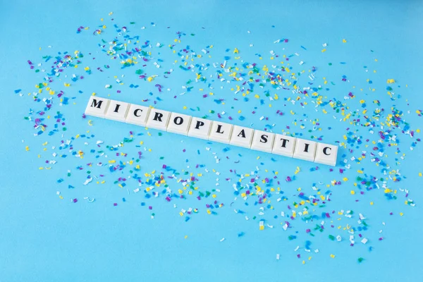 Word MICROPLASTIC around small plastic particles on a blue background. Microplastic in water and food.