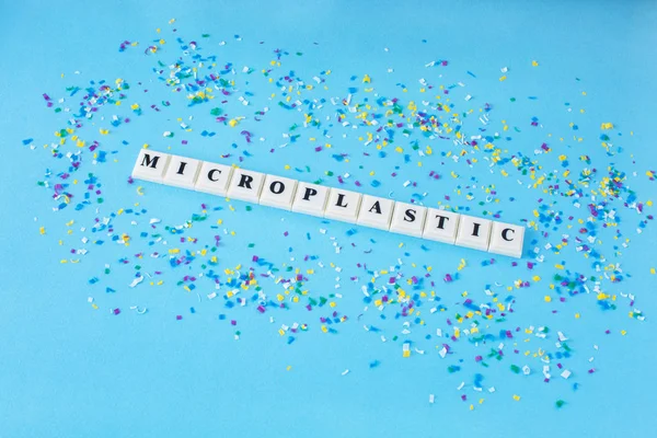 Mavi bir arka plan üzerinde küçük plastik parçacıklar etrafında kelime Microplastic. Microplastic su ve gıda.