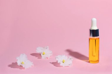 Damlalık cam Şişe Mock-Up. Serum cilt bakım kozmetik ve pembe arka plan, afiş veya şablon üzerinde beyaz narin çiçek. Güzellik ürün konsepti.