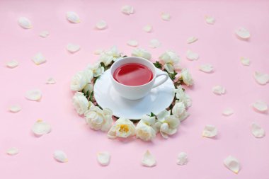 Sevimli beyaz gül ve pastel pembe arka plan üzerinde yaprakları ile çevrili bir fincan çay Üst görüş. Bir fincan çayı kapatın. Düz yatıyordu.