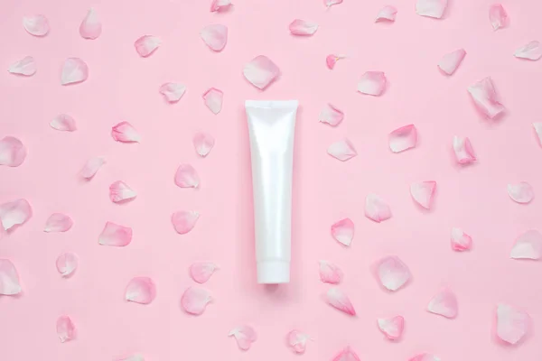 Tubo de plástico brillante blanco con pétalos de flores para medicina o cosméticos, crema, gel, cuidado de la piel, pasta de dientes sobre fondo rosa pastel . — Foto de Stock