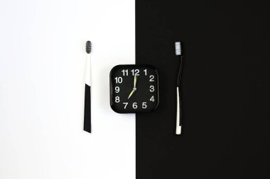 Black alarm clock with manual toothbrush set on white and black background. clipart