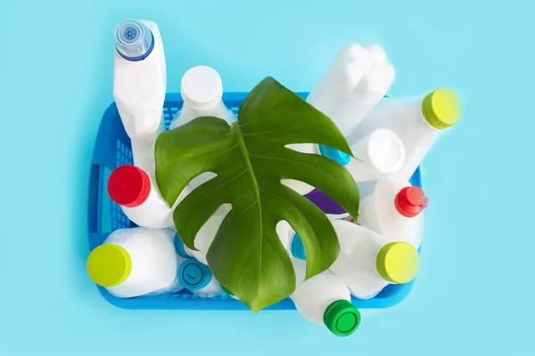 Used Plastic bottles with caps and green leaf in basket for recycling.