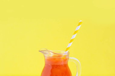 Sarı arka planda kokteyl tüplü bir sürahi havuç suyu. Sağlıklı detoks, alkalin diyeti. Yaz yemekleri konsepti. Metin için alanı kopyala.