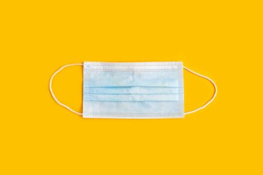 Sarı arka planda lastik kulaklıklı cerrahi maske. Koruma kavramı. Prosedür maskesi..