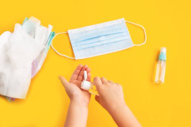 Çocukların elinde sarı arka planda şeffaf el dezenfektanı ve cerrahi maske şişesi var. Çocuk hijyeni. El hijyeni. Bakteri ve virüs koruması. Düz yatıyordu