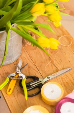 Çiçekçi masası. Çiçekçi çalışma alanı. Makas, kayış takımı, üç çiçek ve havlu. Eski ahşap masa. Çalışan yüzey. Bir buket yap. Hobiler, iş, meslek.