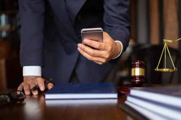 Business lawyers using cell phone for contact customer with brass scale on wooden desk in office. Law, legal services, advice, consult, Justice concept.