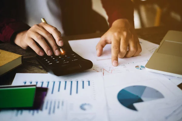 An Accountant man holding pen and using calculator do tax of company on wooden desk in office. freelance, tax, accounting, statistics and analytic research concept.