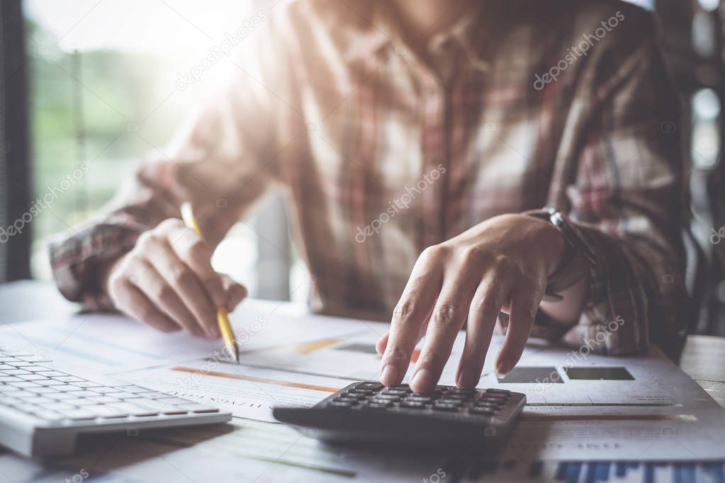 Close up Business woman using calculator and laptop for do math finance on wooden desk in office and business working background, tax, accounting, statistics and analytic research concep