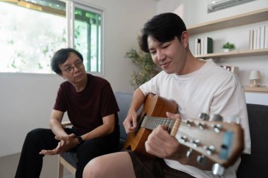 Bir baba, oğlunun gitar çalışını izlerken, sıcak bir ortamda yakın ilişkilerini göstermekten zevk alır..