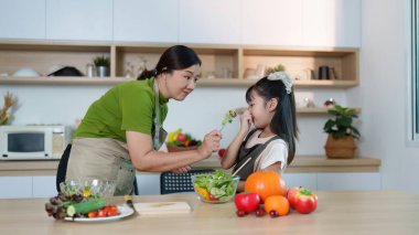 Bir anne taze sebzeler hakkında bilgisini kızıyla paylaşır, şık bir mutfakta sağlıklı beslenmeyi teşvik eder..