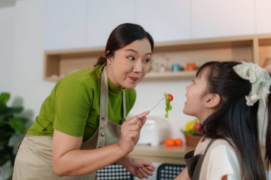 Bir anne ve kızı mutfakta neşeli bir anı paylaşıyor, sağlıklı yemek pişirmenin ve taze malzemelerle kaynaşmanın tadını çıkarıyor..