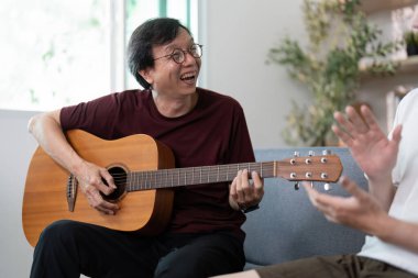 Bir baba oğluyla gülerken gitar çalmaktan zevk alır. Neşeli bağlantılarını ve müzikal bağlarını gösterir..
